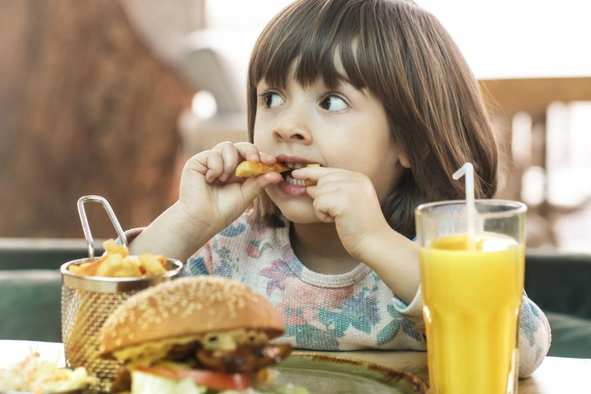 Little girl eating a burger with french fries with orange juice